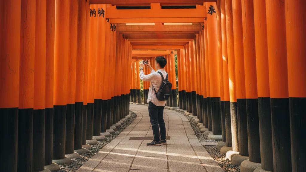 Traveler checking a phone in front of a traditional wooden temple gate at golden hour