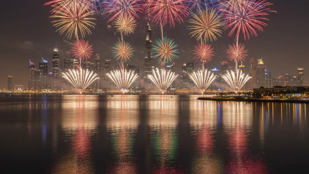 Fireworks bursting over illuminated Dubai skyscrapers and a crowded waterfront promenade during the Dubai Shopping Festival